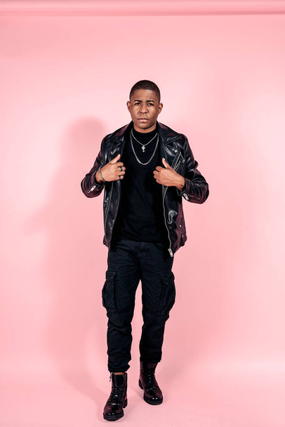 Stock photo of young black man wearing total black look posing in studio shot against pink background. - Фото, зображення