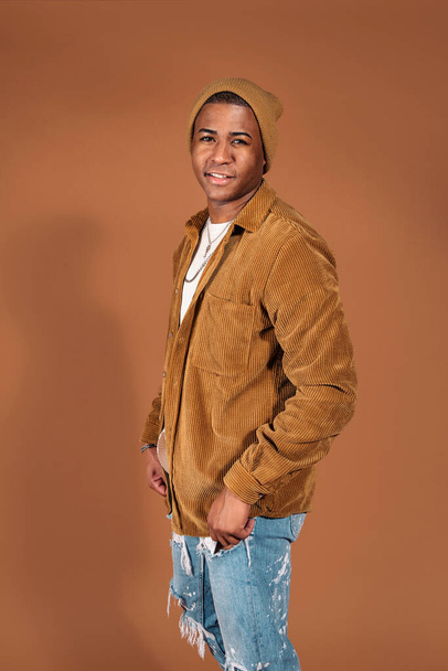 Young man wearing hat smiling in studio shot against brown background. - Foto, Imagen
