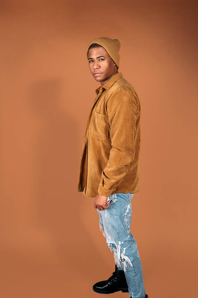 Young man wearing hat posing in studio shot against brown background. - Foto, Imagen