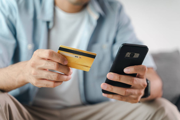 男はクレジットカードを保持し、オンラインショッピング、インターネットバンキング、電子商取引、支出のお金のためのスマートフォンを使用して、家庭の概念から働く - 写真・画像