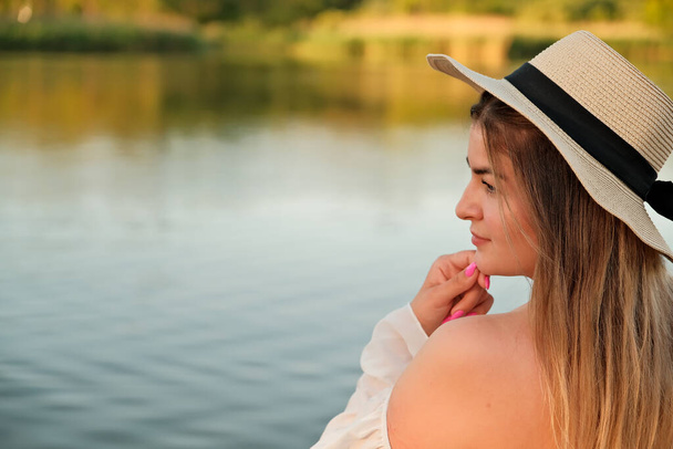 Ein schönes Mädchen mit Hut steht am Ufer. Hut in der Hand. - Foto, Bild