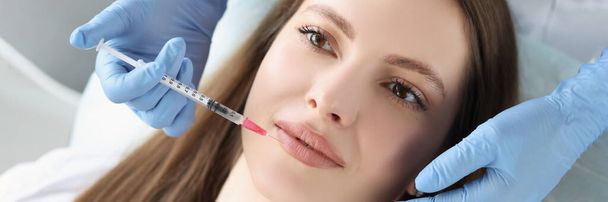 A fiatal nő arcképe botox injekciót kap az ajkába, a kozmetológus fecskendőt használ. Kozmetológia, szépségápolás, plasztikai sebészet, klinika koncepció - Fotó, kép