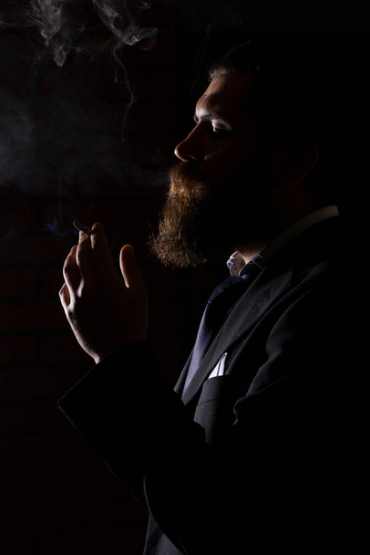 Man smoking cigarette isolated on black. A man smokes cannabis weed, a joint and a lighter in his hands. Smoke on black background. Concepts of medical marijuana use and legalization of the cannabis - Foto, Bild