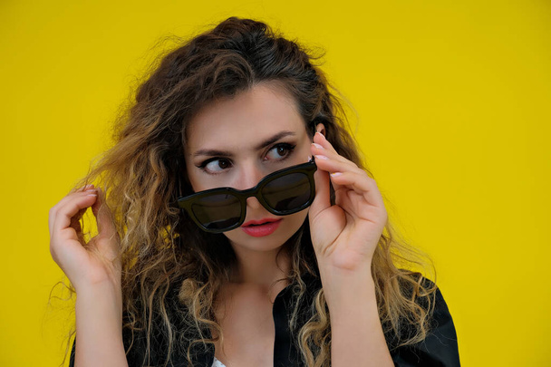 Close-up portrait of a beautiful girl on a yellow background. a woman in black glasses looks thoughtfully. human emotions - Fotó, kép