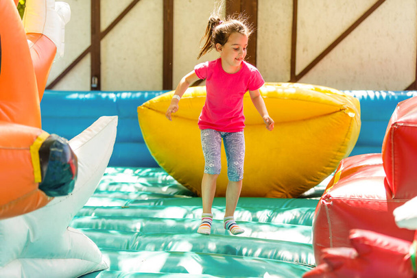 Happy little girl having lots of fun on a jumping castle during sliding - Photo, Image