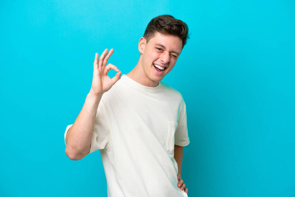 Young handsome Brazilian man isolated on blue background showing ok sign with fingers - Фото, изображение
