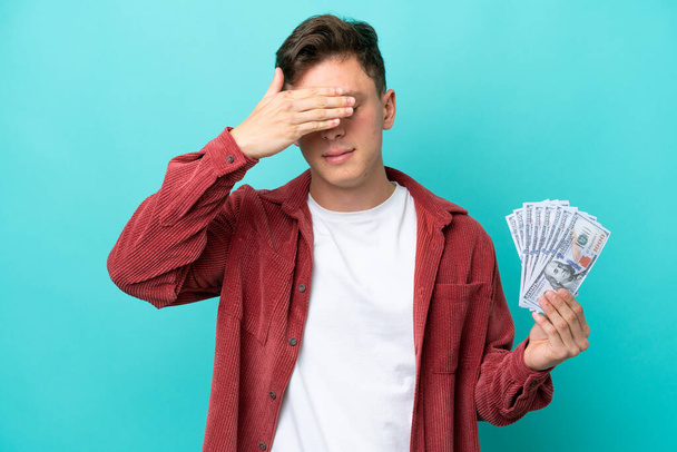 Young brazilian man taking a lot of money isolated on blue background covering eyes by hands. Do not want to see something - Photo, Image
