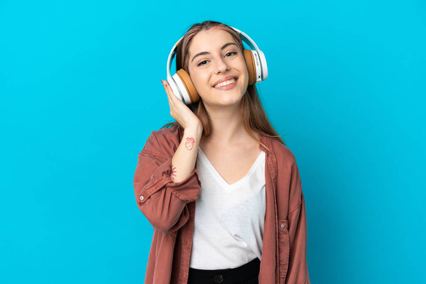 Young caucasian woman isolated on blue background listening music - Foto, Imagem