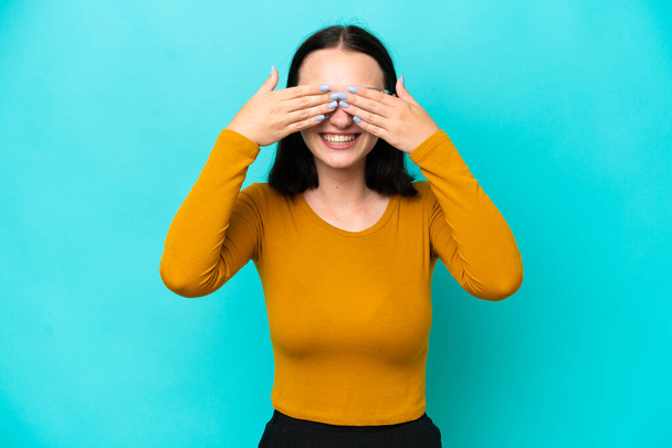 Young caucasian woman isolated on blue background covering eyes by hands and smiling - Zdjęcie, obraz