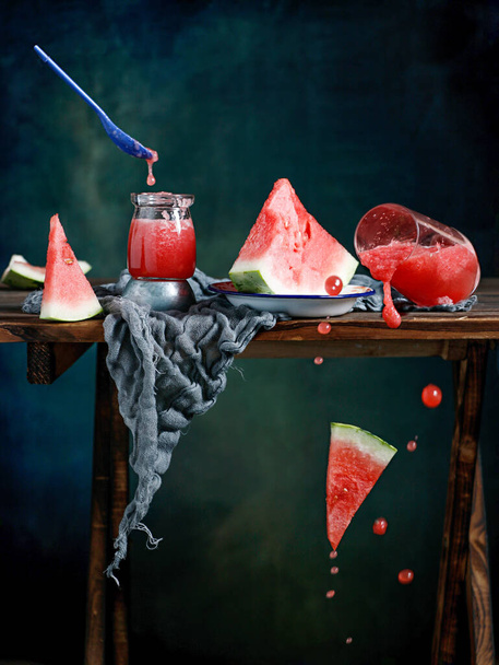 A closeup shot of watermelon glass juice and a cup spilling with watermelon slice falling on the table - Foto, Imagen