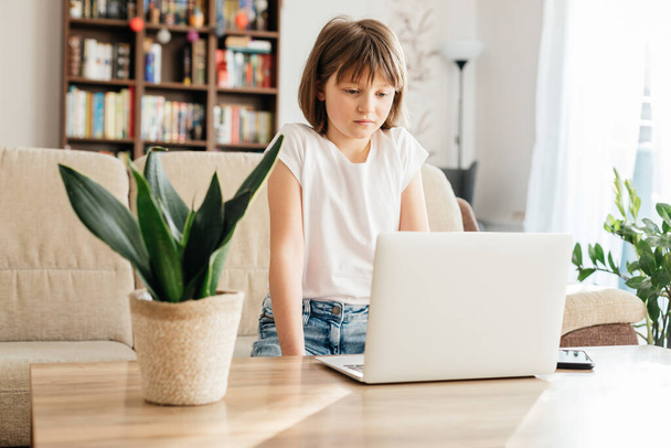 Distance learning. The girl sits at home on the couch and studies using a laptop or makes calls and watches lessons. Children use technology. - Φωτογραφία, εικόνα