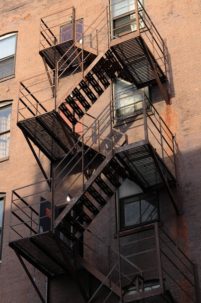 A vertical shot of a building with fire escape stairs on the exterior of the building - Фото, зображення