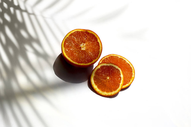A closeup of ripe juicy orange slices on a white background with shadows of leaves - 写真・画像