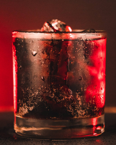 Un primer plano vertical de una bebida de soda con cubitos de hielo sobre un fondo de neón rojo - Foto, imagen