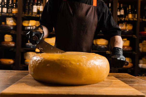 Roue de fromage jaune vieilli naturel maasdam limitée coupée en deux avec un couteau sur la table. Fromage en magasin. Snack savoureux morceau de fromage pour l'apéritif - Photo, image