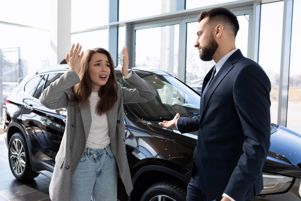 απογοητευμένη νεαρή γυναίκα σε μια αντιπροσωπεία αυτοκινήτων ουρλιάζοντας χειρονομίες gesturing με τα χέρια. - Φωτογραφία, εικόνα