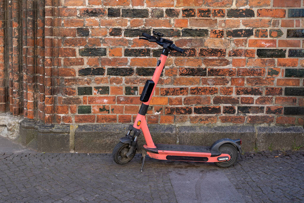 A pink electric scooter parked next to a brick wall - Foto, immagini
