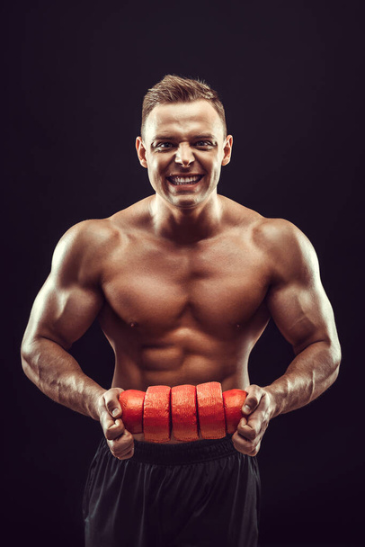 Power, strength, excellent body, bodybuilding, sports concept. Young handsome muscular fit man demonstrating perfect body and hold circles of cheese in orange wax.  - Zdjęcie, obraz