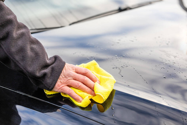 A hand with yellow rag cleaning the hood of a black car - Fotó, kép
