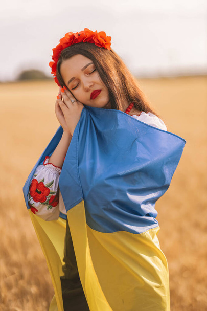 Молода сумна дівчина накрилася на прапорі, чекаючи на перемогу в полі, одягнена в українську національну вишиту сорочку з червоним вінком. Концепція незалежності України, свободи і припинення війни. Мир у слові - Фото, зображення