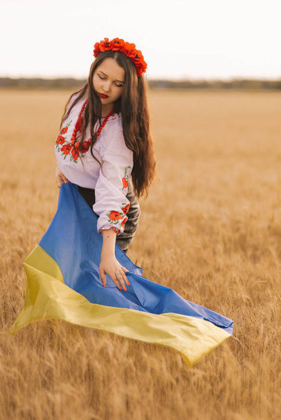 Genç kız buğday tarlasında bayrağa dokunuyor Ukrayna ulusal nakışlı gömleği ve çiçekli kırmızı çelenk ve kolye giyiyor. Bağımsızlık kavramı, Ukrayna 'nın özgürlüğü ve savaşı durdurmak. Kelimelerle barış - Fotoğraf, Görsel