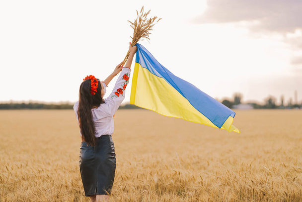 Sahada zaferi bekleyen genç bir kız Ukrayna ulusal nakışlı kırmızı çelenkli gömlek giyiyor ve elinde bayrak ve buket tutuyor. Bağımsızlık kavramı, Ukrayna 'nın özgürlüğü ve savaşı durdurmak. - Fotoğraf, Görsel