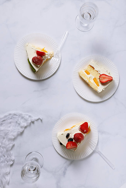 A top view shot of three plates with strawberry cake pieces on a white surface - 写真・画像