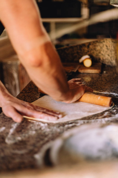 Male hands rolling out dough for pizza on a table - Fotó, kép