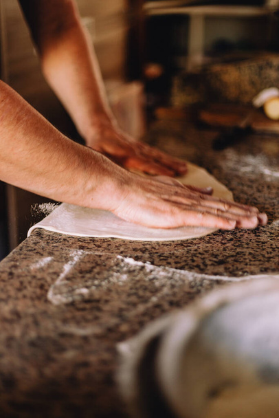 Male hands stretching dough for pizza on a table - Foto, imagen
