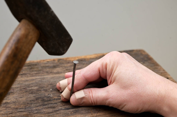 A male hand with stitches on fingers fixing the nail on the wood and hitting it with a hammer - Foto, immagini