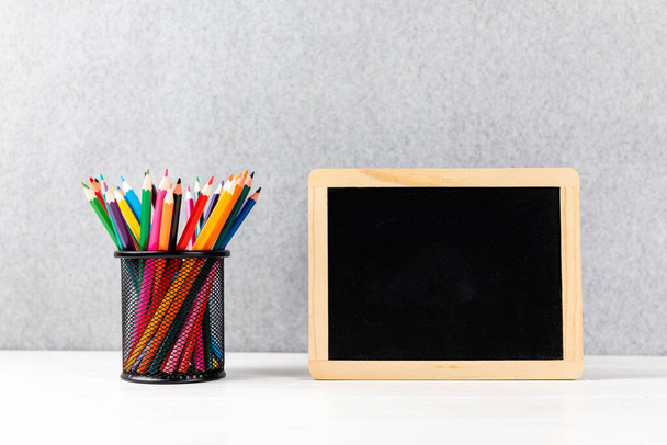A closeup of colorful pencils and chalkboard on a desk with gray background and copyspace - Foto, Bild