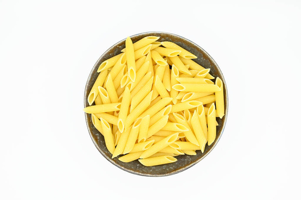 A top view of raw penne pasta on a white background - Фото, изображение