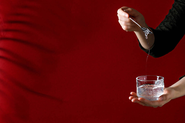 A girl holding a cup with cold liquid and stiring with a spoon near red wall with copy space - Fotografie, Obrázek
