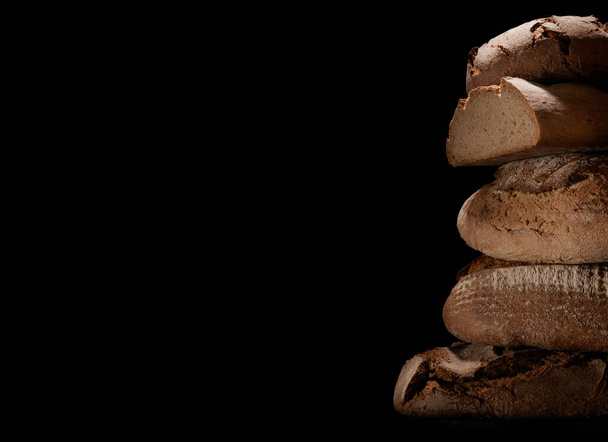 A closeup of fresh-baked loaves stacked on top of each other against a black background - Photo, Image