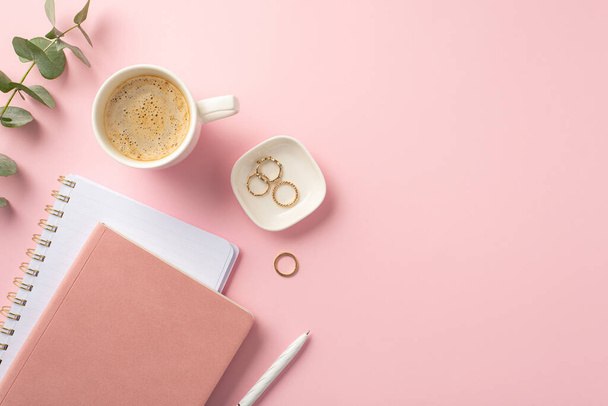 Business concept. Top view photo of workplace pink reminders pen gold rings cup of coffee and eucalyptus sprig on isolated pink background with empty space - Photo, Image