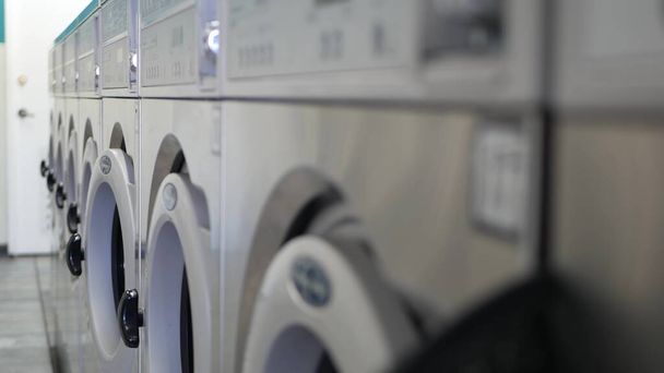 Row of washing and drying machines, public coin laundry in California, USA. Drums of washers and dryers in self-service laundromat or commercial laundrette. Automatic launderette in United States. - Photo, Image