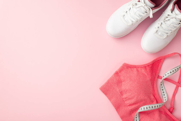 Concetto fitness. Foto vista dall'alto di scarpe da ginnastica bianche rosa reggiseno sportivo e metro a nastro su isolato sfondo rosa pastello con copyspace - Foto, immagini