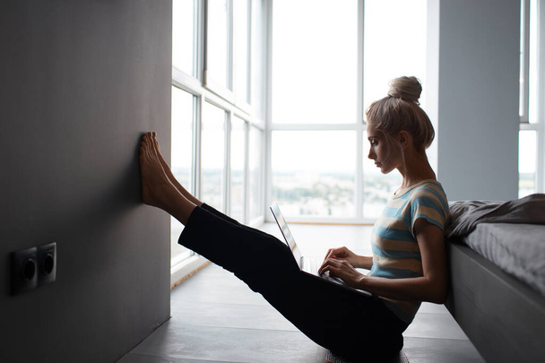 Blonde girl with hair bun working home, typing on laptop, sitting on the floor. - Photo, Image