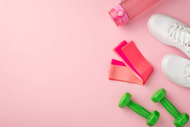 Fitness-Zubehör-Konzept. Foto von oben von weißen Turnschuhen rosa Flasche Wasserwiderstandsbänder und grüne Hanteln auf isoliertem pastellrosa Hintergrund mit Kopierraum - Foto, Bild