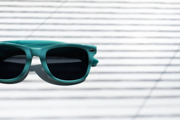 Primer plano de medias gafas de sol de color azul sobre fondo blanco rayado por sombras. - Foto, Imagen
