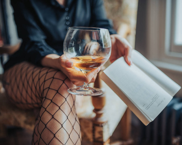 ウイスキーと本のガラスを持っている網のストッキングを身に着けているセクシーな女性 - 写真・画像