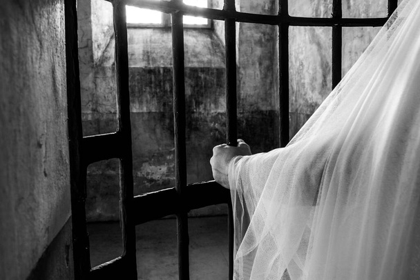 A grayscale shot of a person wearing a bride dress and catching metal cells in a dark moist place - Foto, immagini