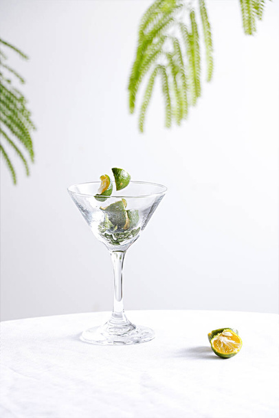 A vertical shot of a lime pieces floating over a glass of alcoholic cocktail on a white table - Foto, imagen