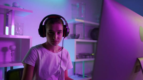 Closeup beautiful girl gamer in neon lights at home. Focused esport professional looking in camera. Focused player streamer using powerful pc in headset. Serious woman playing online arcade game.  - Foto, Bild