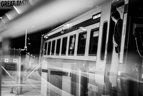 A grayscale of a man standing between doors of a train at the metro station with long exposure effect - 写真・画像