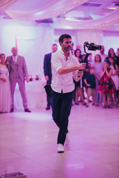 A videographer in a white shirt filming a wedding party in a restaurant - Fotó, kép