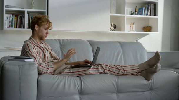 Freelancer talking home online resting in pajamas. Ginger man working remotely. Focused businessman videocalling company team enjoying virtual meeting. Business analyst consult client on quarantine - Photo, Image