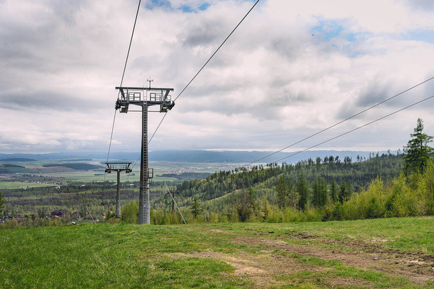 A vertical shot of ski lift over field and forest under a cloudy sky during daytime - Photo, image