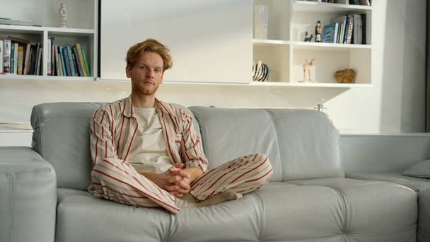 Single guy resting sofa in morning. Pensive businessman considering problems at home. Serious ginger freelancer take break relaxing in lotus position on comfortable couch. Millennial man posing alone - Photo, Image