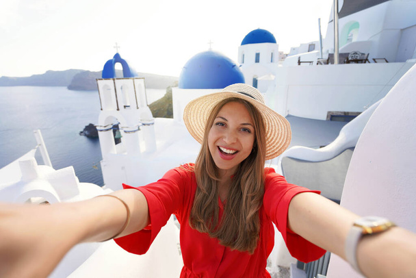 Chica viajera emocionada tomando foto selfie en Santorini al atardecer. Mujer joven divirtiéndose en el pueblo pintoresco de Oia en Grecia. - Foto, imagen